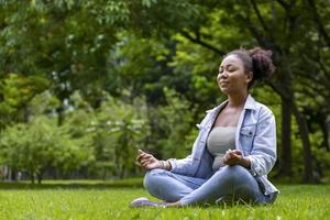 afroamerikansk kvinna som avkopplande övar meditation i skogen för att uppnå lycka från inre frid visdom för friskt sinne och själ foto