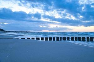 solnedgång på stranden av Östersjön. hoppor når ut i havet. blå timme foto