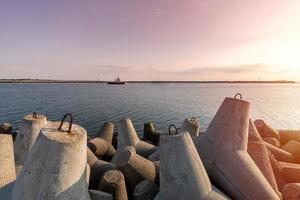 fartyg-bogserbåt går i öppet hav för att bogsera lastfartyg till hamn. vacker solnedgång över piren. tetrapod vågbrytare i hamnen. foto