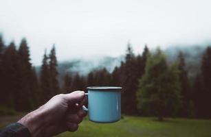 blå kopp i händer med skog bakgrund. filmisk resa inspirerande bakgrund foto