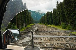 främre fönstret visa skogen i naturen på roadtrip reser med hyrbil koppla av baksätet ta foto passagerare. livsstil semester vibbar utomhus lynniga berg utsikt öppet fönster