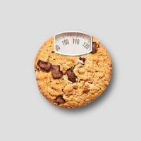 chocolate chip cookie som en viktskala på grå bakgrund. diet koncept. toppvy. minimalt matkoncept. collage gjord av chokladkaka och viktvåg. samtida konstcollage. foto
