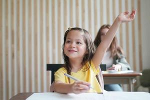 förskola flicka kid rita med färgpenna på vitt papper på bordet i klassrummet med vänner foto