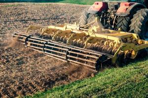 traktor kultivator plöjer marken, förbereder för grödor. damm på fältet foto