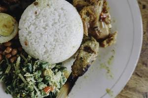 nasi campur ayam betutu. balinesisk stekt kyckling fylld med kassavablad. tillsammans med ångat ris, sate lilit, jukut antungan, lawar nangka och sambal matah. foto