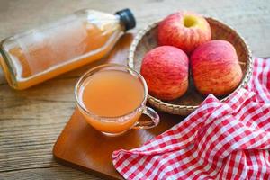 äppelcidervinäger naturliga botemedel och botemedel för vanligt hälsotillstånd, rå och ofiltrerad organisk äppelcidervinäger i glas med äppelfrukt på korgen på träbordet foto