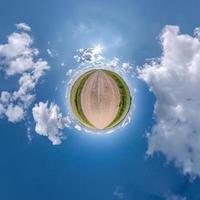 liten planet i blå himmel med sol och vackra moln. transformation av sfäriskt panorama 360 grader. sfärisk abstrakt flygfoto. utrymmets krökning. foto
