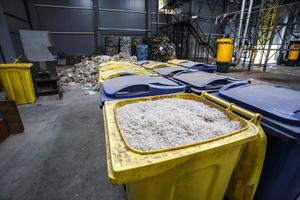 behållare med strimlad plast förberedda för vidarebearbetning omsmältning och återvinning med rivare och balar med plastavfall i bakgrunden. modern anläggning för bearbetning och sortering av sopor foto
