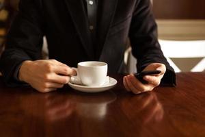 man dricker kaffe och använder en mobiltelefon.