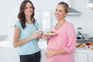 smilande gravid kvinna som håller kakor och hennes vän