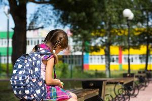 ledsen, upprörd tjej nära skolan med en ryggsäck. trötthet från lektionerna, förbittring, lärdomar som inte har dragits, dåligt betyg. tillbaka till skolan. kopieringsutrymme foto