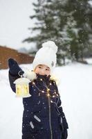 ett barn på vintern på en snöig gata under ett snöfall i en glödande krans med stjärnor. förberedelse för julhelgen, nyår. festlig stämning, förväntan på ett mirakel foto