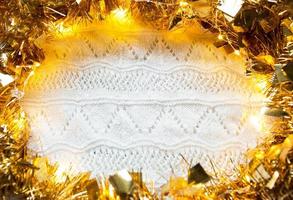 festlig ram gjord av guldgirlang med lampor och glitter på en vit stickad med mönsterbakgrund, copyspace. nyår, jul, höst och vinter värmande atmosfär. foto