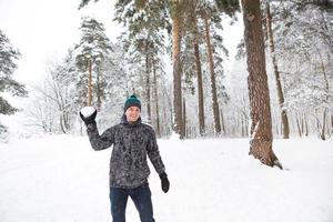 en ung man med en snöboll i handen har roligt och svänger för ett kast. vinter familj och vänliga spel och underhållning i skogen med snö i det fria foto
