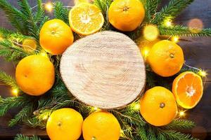 nyårshelgdagbakgrund på rund skärning av träd omgiven av mandariner, levande grangrenar och gyllene ljusgirlanger, med träutrymme för text. citrusarom, apelsinskivor, jul. ram foto