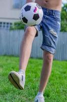 ung man i jeansjeans och vita sneakers som spelar fotboll utomhus. amatör fotbollsspelare mint bollen foto