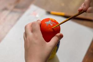 liten pojke målar rysk häckande docka som heter matrioshka med röd och gul färg foto