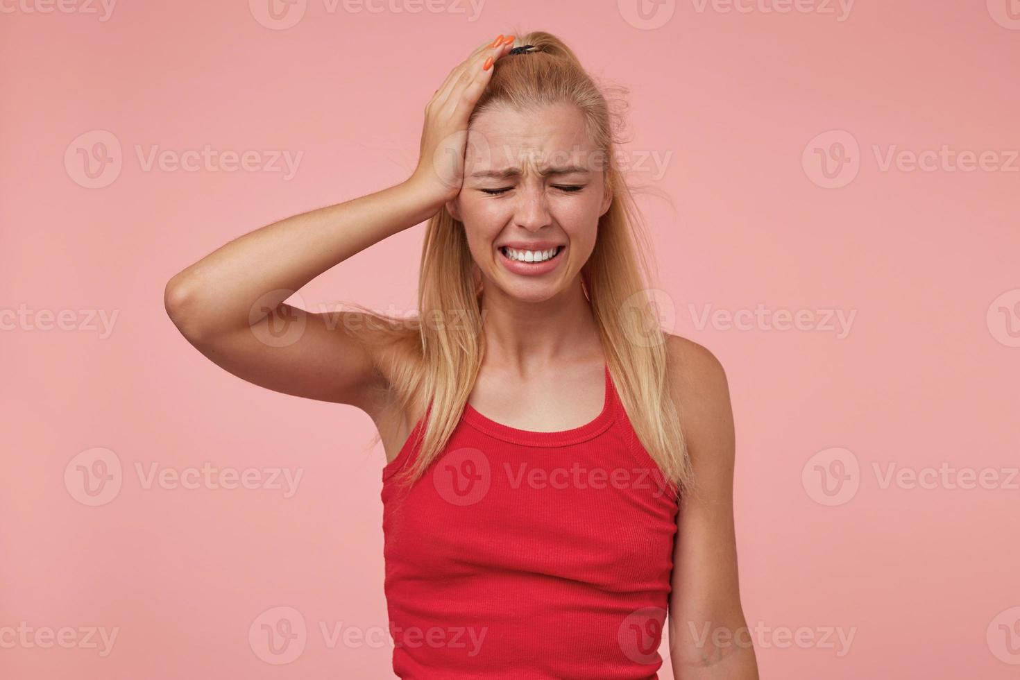 mooie langharige blonde vrouw in vrijetijdskleding poseren over roze achtergrond met pijnlijk gezicht, handpalm op haar hoofd houdend, lijdend aan hoofdpijn foto