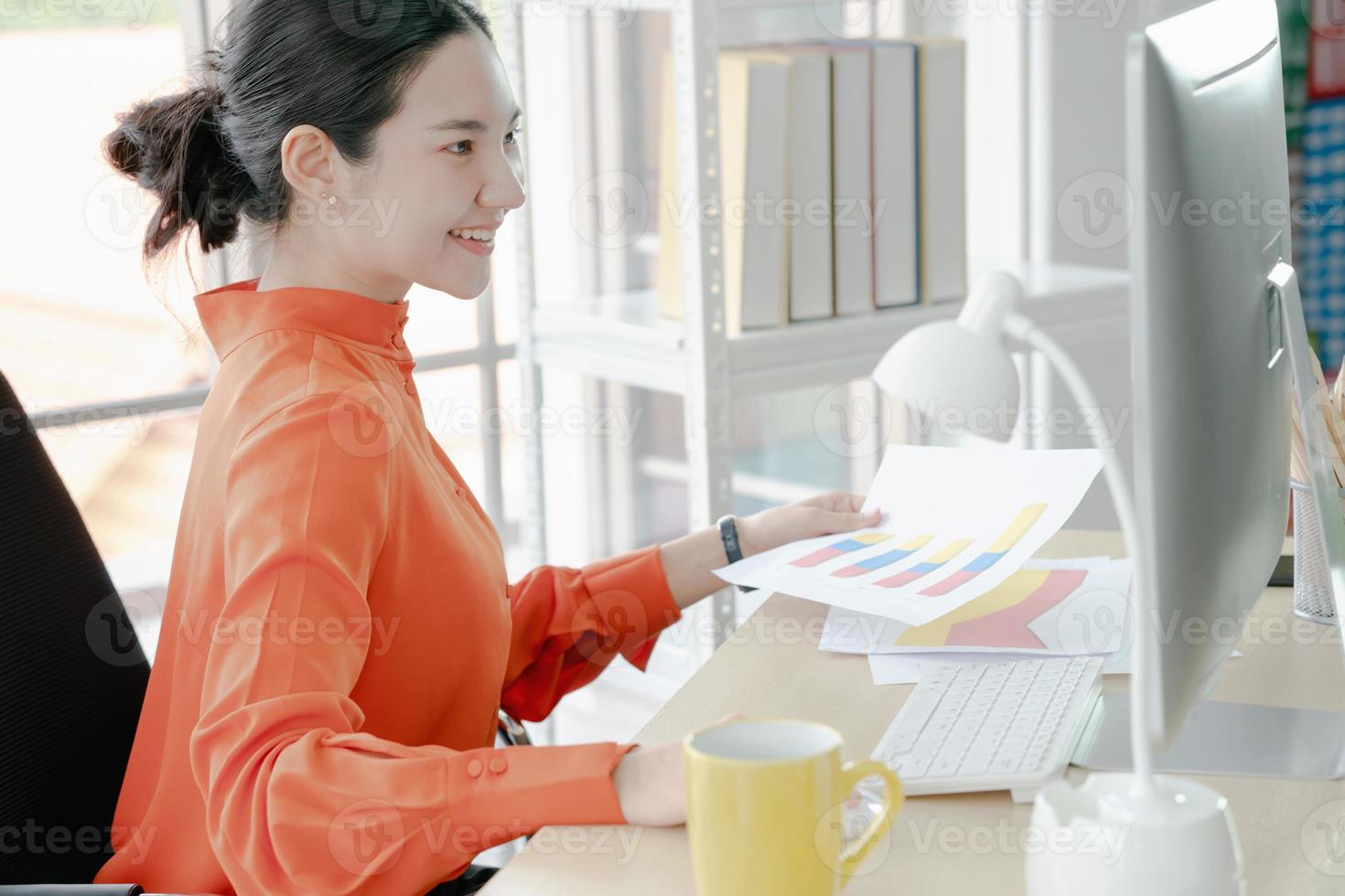 vrouwelijke directeur die op kantoor aan het bureau zit en bedrijfsstatistieken analyseert met diagrammen en grafieken met behulp van de computer foto