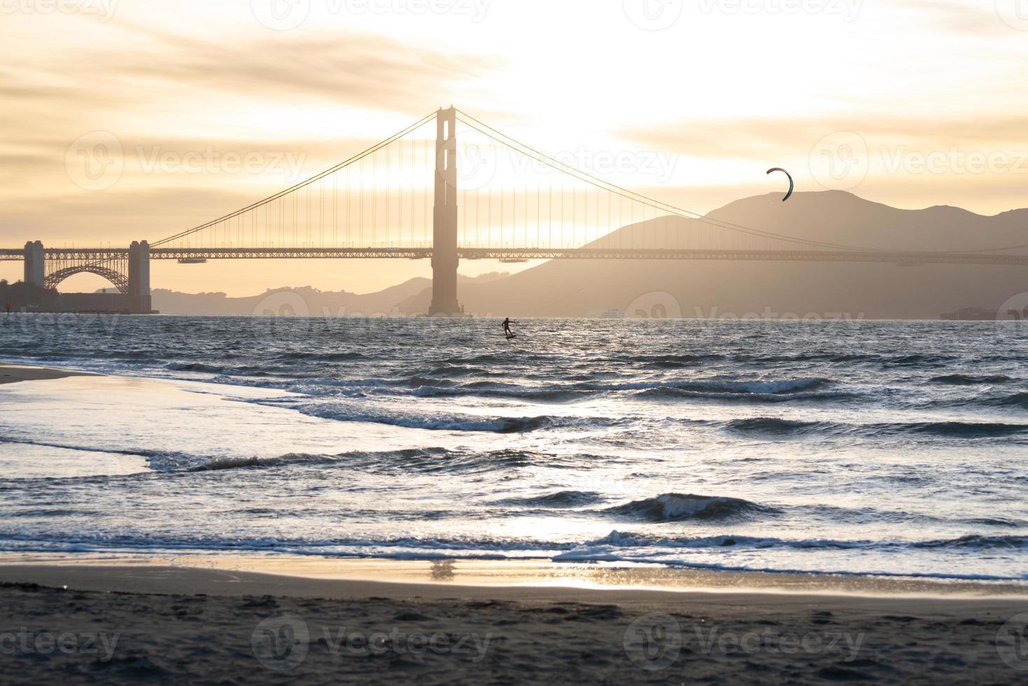 golden gate bridge in de schemering met een goudbruine pastelkleurige lucht en een omtrek van een kitesurfer foto