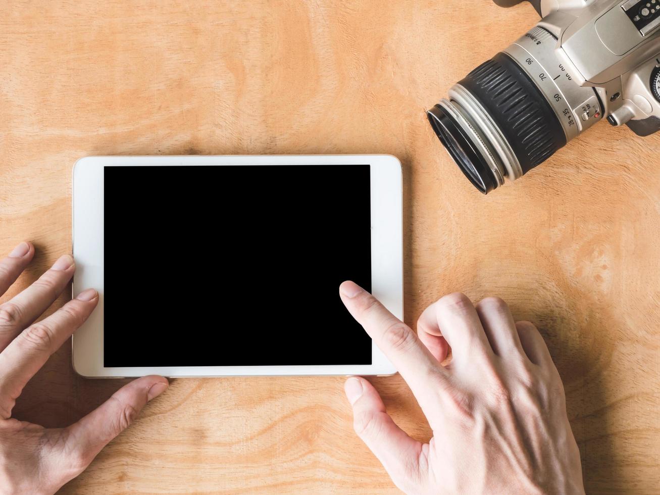 bovenaanzicht van mannelijke handen met behulp van tablet met camera op houten tafel. foto