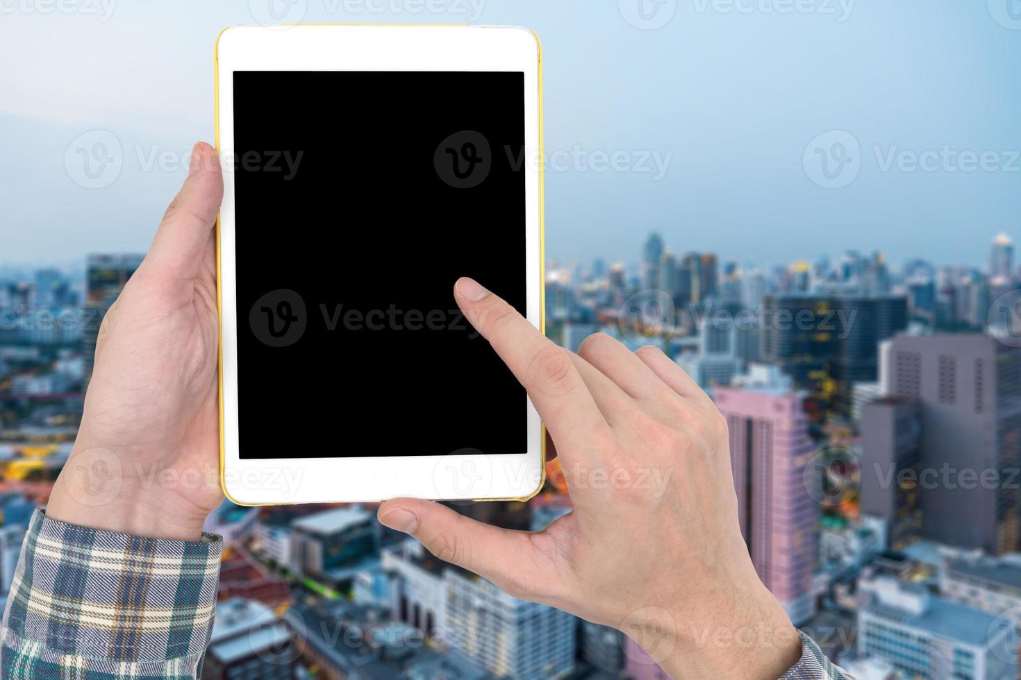 mannelijke handen met een witte tablet-aanraakcomputergadget met een leeg zwart scherm op de wazige achtergrond van het stadslandschap. foto