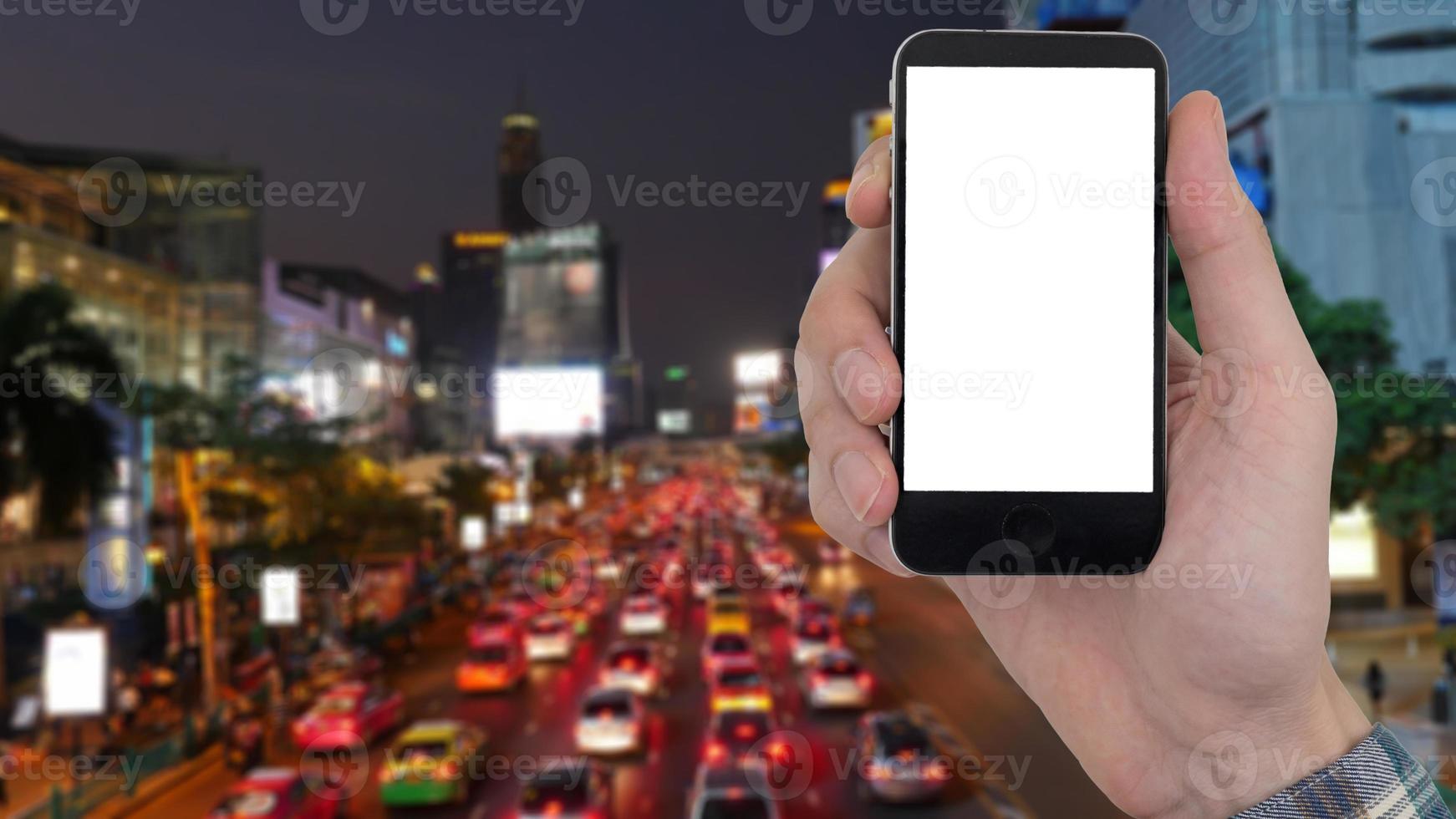 mannelijke hand met een mobiele telefoon met een leeg wit scherm op de wazige achtergrond van het stadslandschap. foto