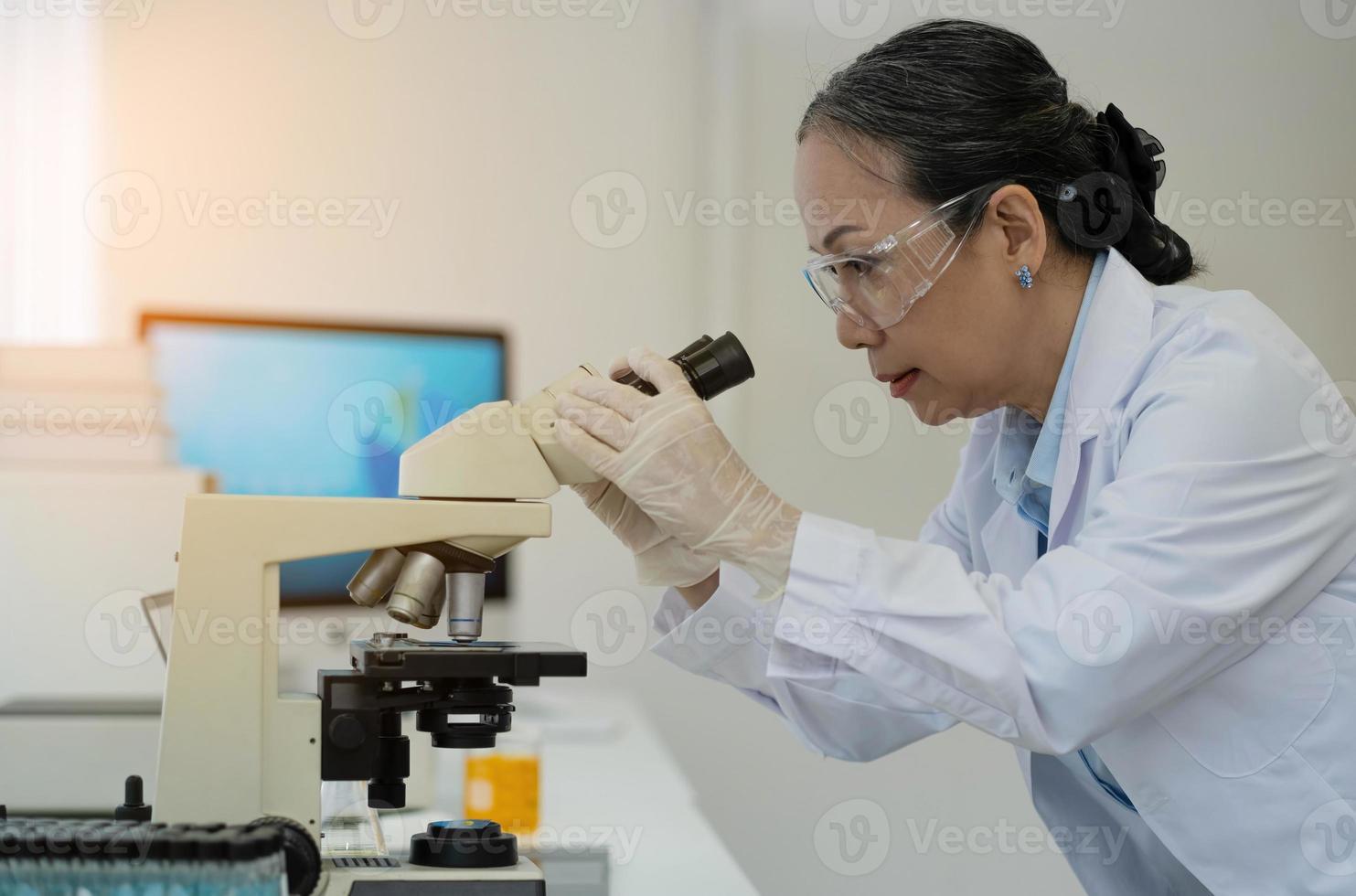 medisch ontwikkelingslaboratorium vrouwelijke wetenschapper die onder de microscoop kijkt, analyseert petrischaalmonster. op de achtergrond groot farmaceutisch laboratorium met specialisten die medicijnen leiden foto