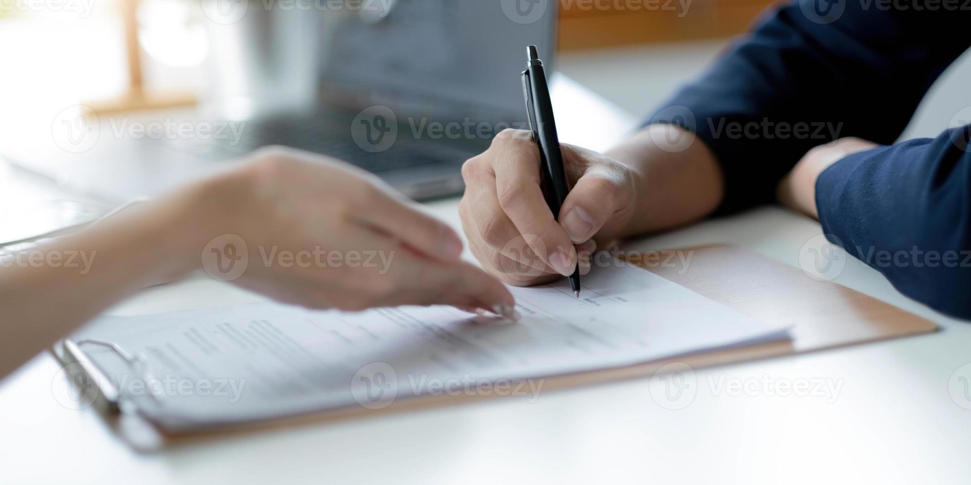 close-up van de hand van de oude vrouw die een medisch verzekeringscontract ondertekent op het kantoor van de dokter. vrouwelijke dokter laat gepensioneerde dame cliënt plaats zien om handtekening te zetten op zorgverzekeringspolis foto