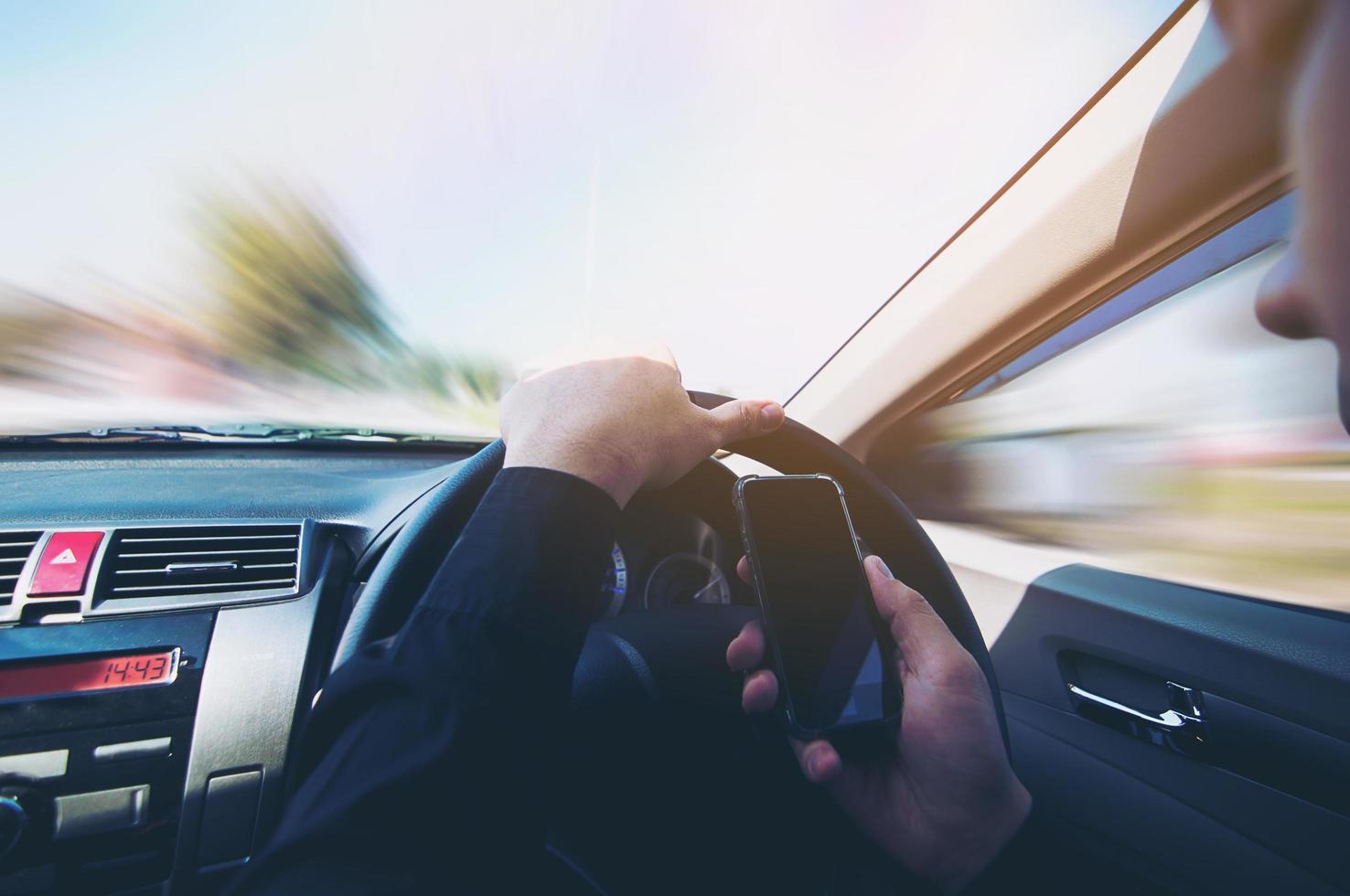 close-up van een man die gevaarlijk auto rijdt tijdens het gebruik van een mobiele telefoon foto