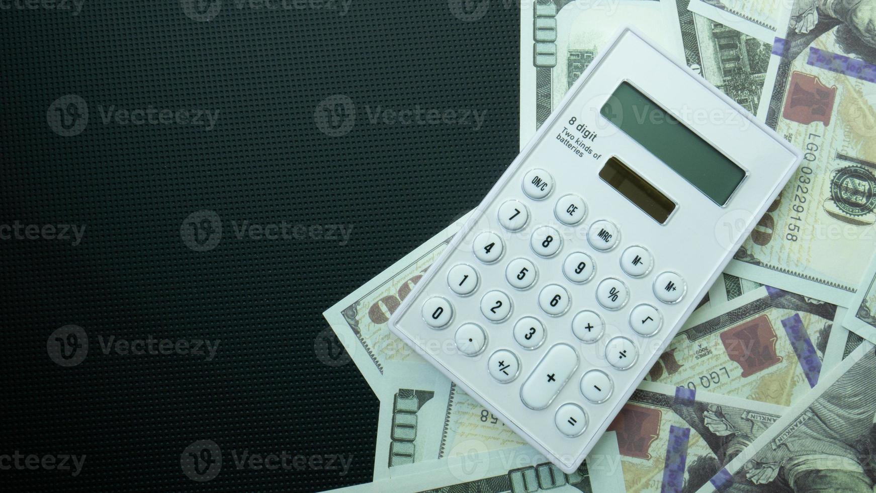 het bankbiljet van 100 dollar en de rekenmachine op zwarte achtergrond voor zakelijke inhoud foto