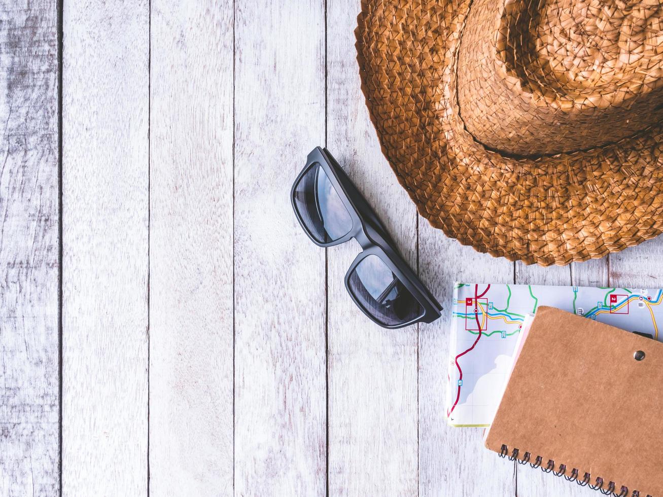 bovenaanzicht van zonnebril, hoed, notitieboekje en kaart op houten tafel. reisconcept foto
