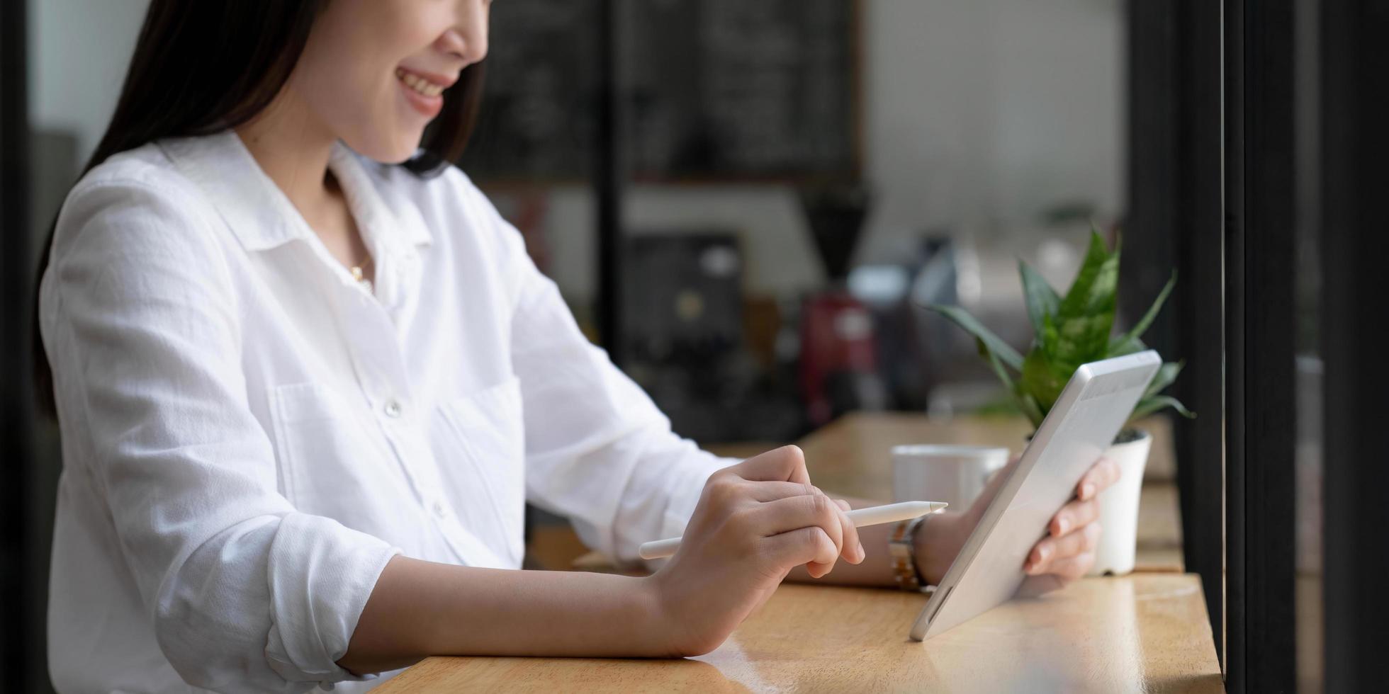 mooie jonge aziatische vrouw of vrouwelijke student ontspant zittend in de coffeeshop en het gebruik van draagbare tablet-touchpad. foto