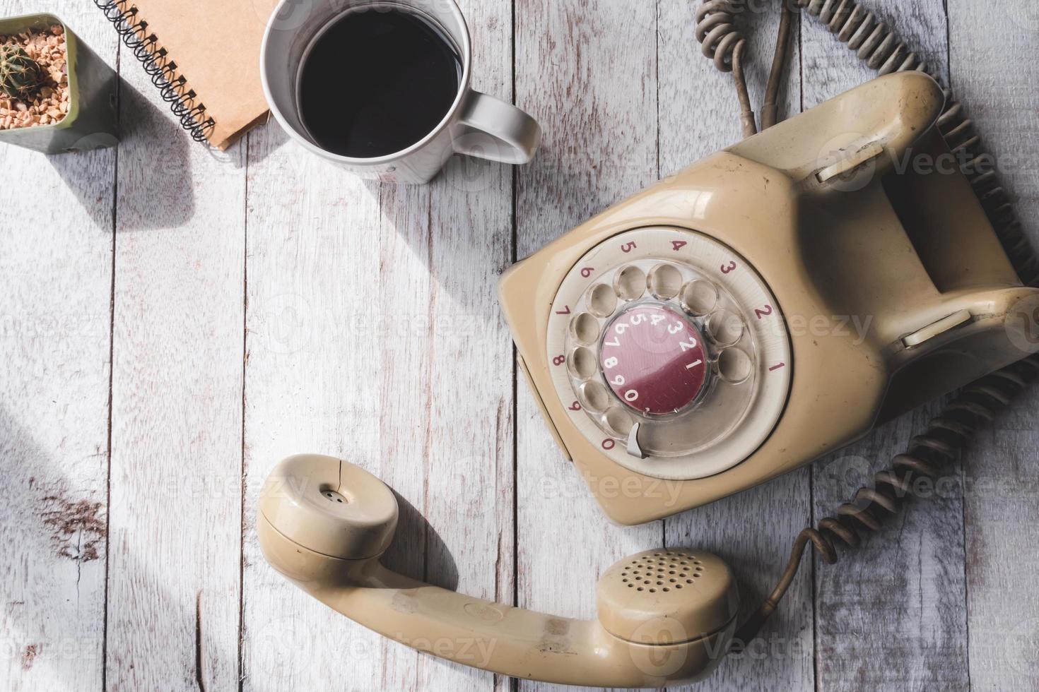 bovenaanzicht van oude telefoon met koffiekopje, notebook en cactus op witte houten tafel achtergrond. foto