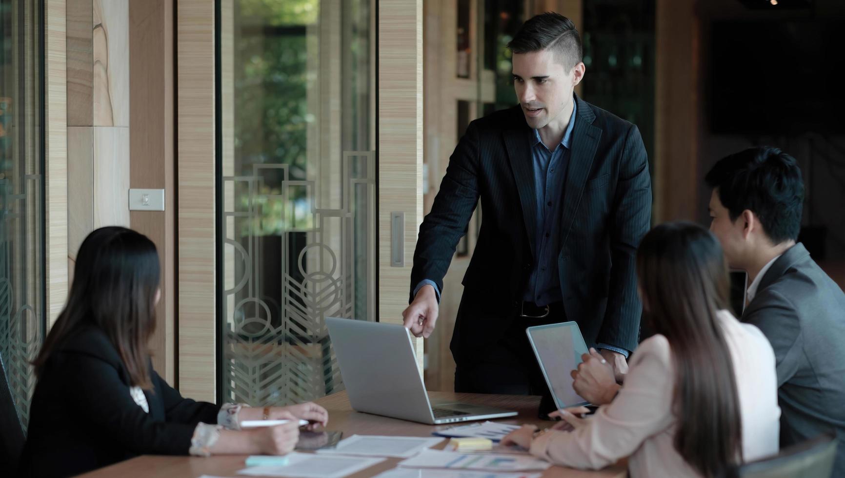 zakenmensen die teamwerk tonen tijdens het werken in de bestuurskamer in het kantoorinterieur. mensen die een van hun collega's helpen om een nieuw businessplan af te ronden. bedrijfsconcept. teamwerk. foto