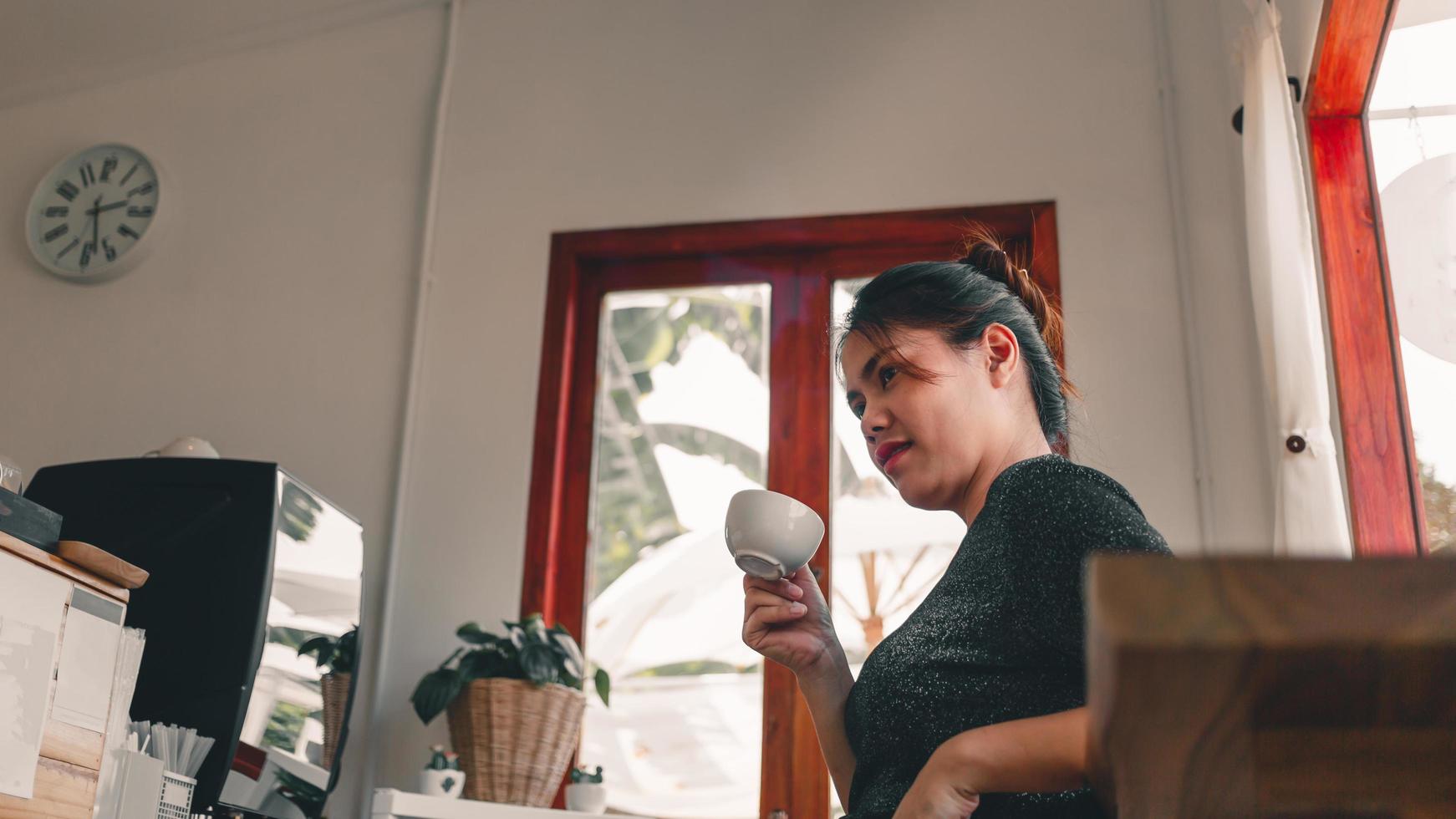 mooie aziatische vrouw gaat zitten aan de bar in een koffiebar bij het raam met een kopje koffie, glimlachend ontspannen in een café foto