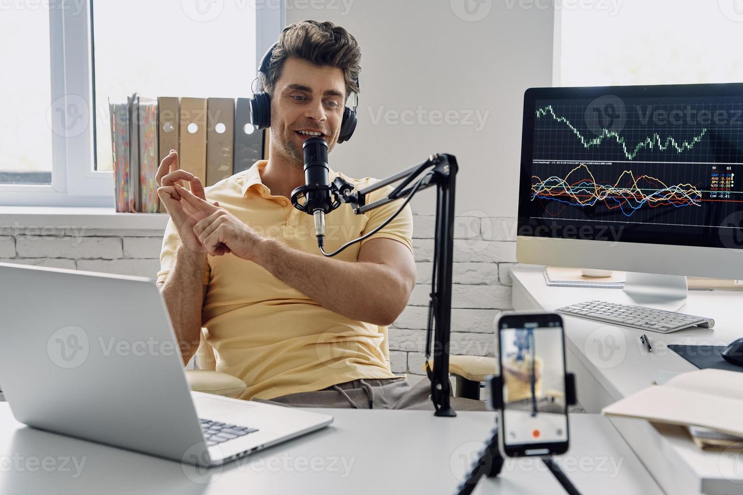 jonge man in koptelefoon met microfoon en gebaren tijdens het opnemen van zijn zakelijke podcast foto