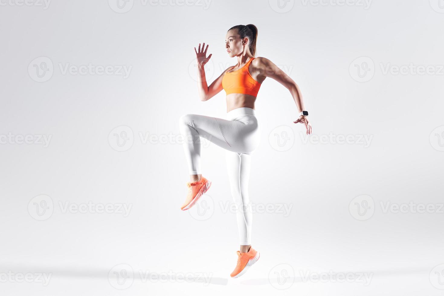 aantrekkelijke jonge vrouw in sportkleding die tegen een witte achtergrond springt foto