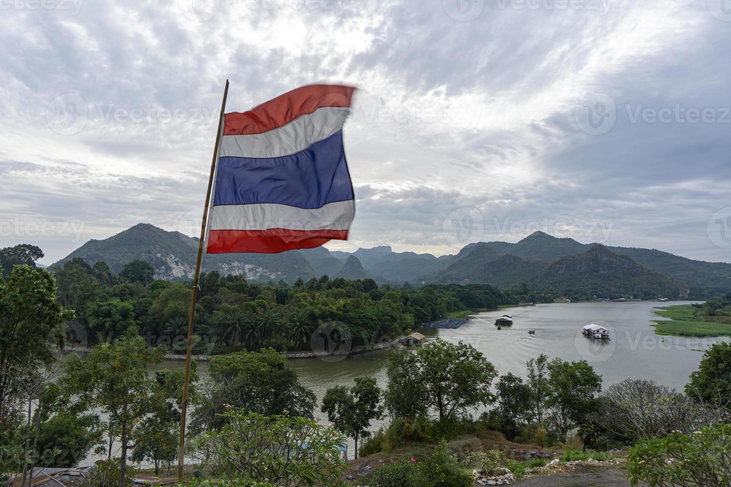 thaise vlag geblazen uit de wind, de achtergrond is het uitzicht op de rivier kwai en de bergen van kanchanaburi, thailand foto