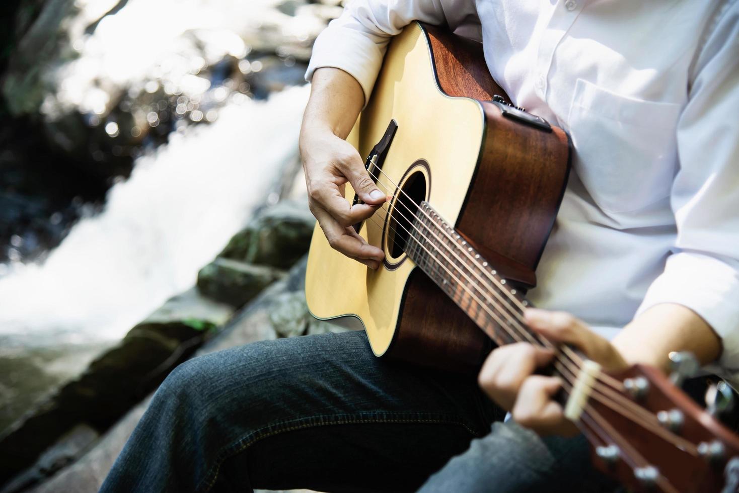 man speelt ukelele nieuw voor de waterval - mensen en muziekinstrument levensstijl in natuurconcept foto