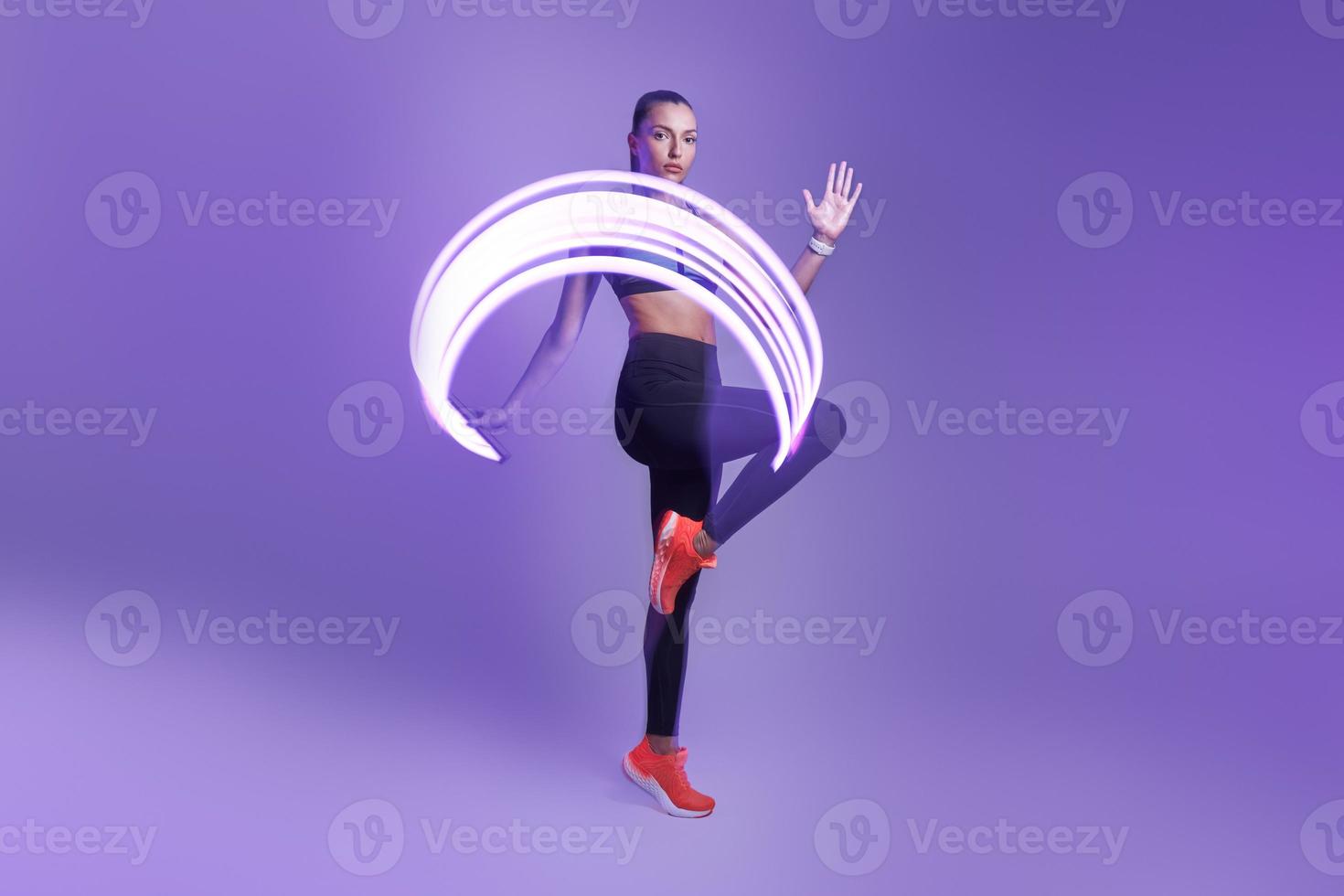 zelfverzekerde jonge vrouw in sportkleding die traint tegen een violette achtergrond foto