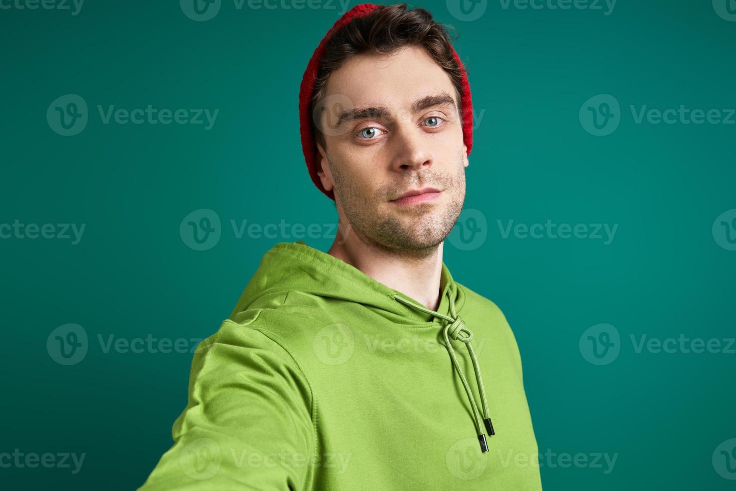 knappe jonge man die selfie maakt terwijl hij tegen een groene achtergrond staat foto