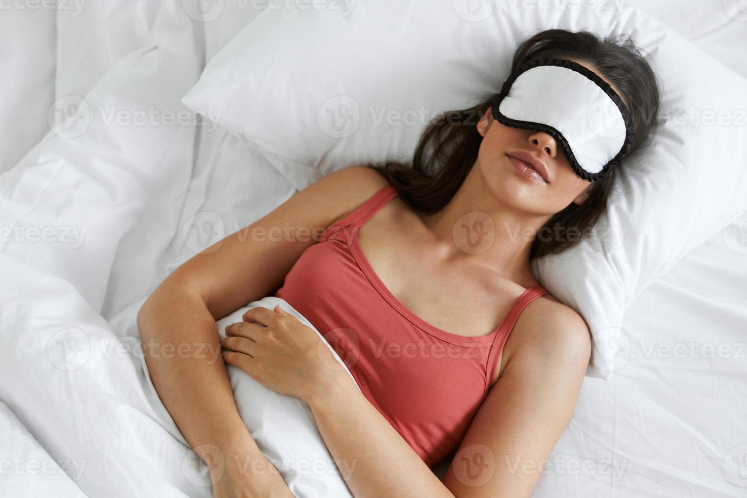 bovenaanzicht van een mooie vrouw die een slaapmasker draagt terwijl ze in bed ligt foto