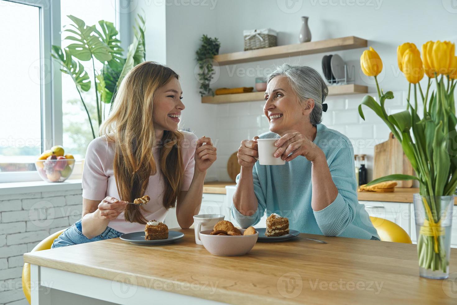 senior moeder en haar volwassen dochter genieten van warme dranken en zoet eten in de keuken foto