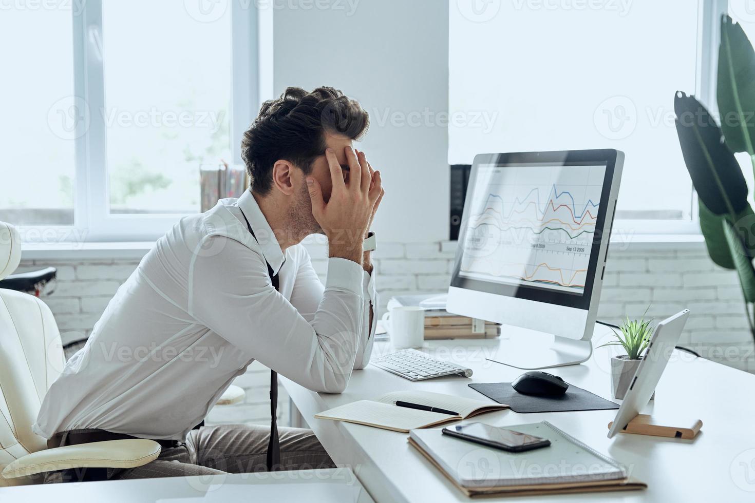 depressieve jongeman die zijn gezicht bedekt met handen terwijl hij op zijn werkplek op kantoor zit foto