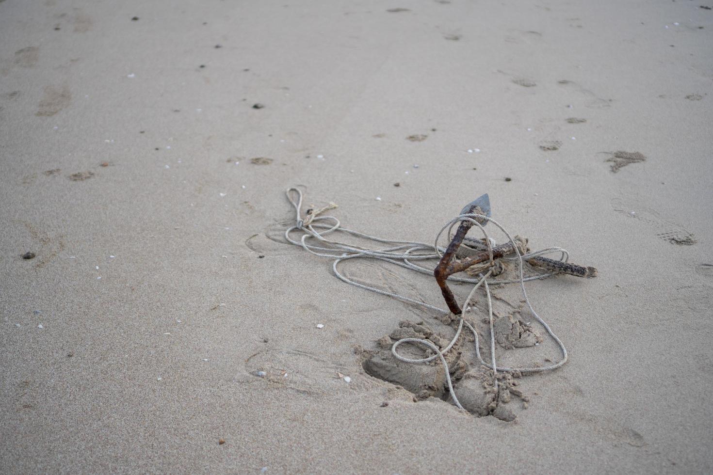 een klein anker verroest op het zand van het strand aan zee foto