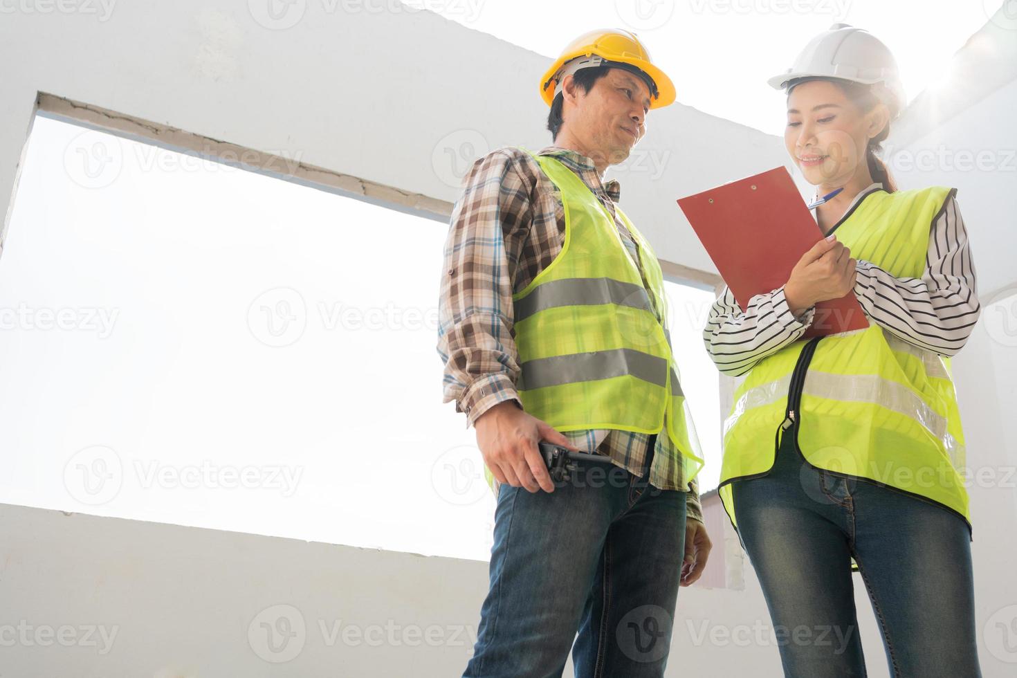 Aziatische ingenieur of jonge vrouwelijke architect zet een helm op voor veiligheid en praat met een aannemer over een bouwproject voor een fabrieksgebouw, concept van teamwork, leiderschapsconcept. foto