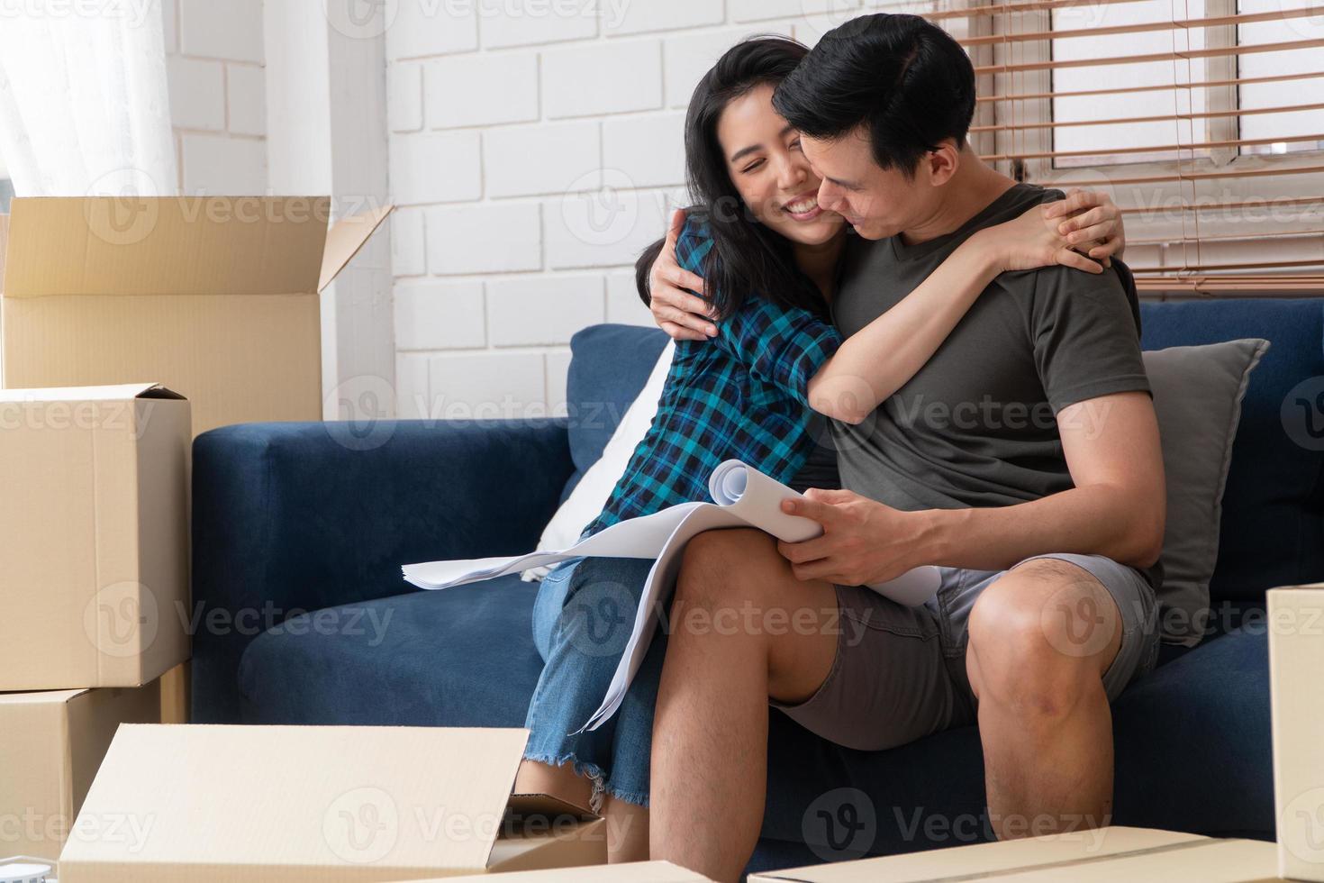 glimlachend jong aziatisch gelukkig stel houdt een blauwdruk vast voor ideeën voor huisdecoratie op de verhuisdag in hun nieuwe huis na het kopen van onroerend goed. concept van het starten van een nieuw leven voor een pas getrouwd stel. foto