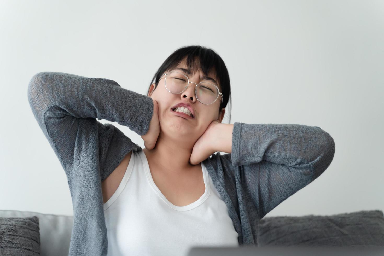 vermoeide gestresste zakenvrouw die lijdt aan fibromyalgie nekpijn die thuis op de bank werkt. overwerkte jonge dame die nek masseert gevoel gekwetst pijn van zittend werk foto