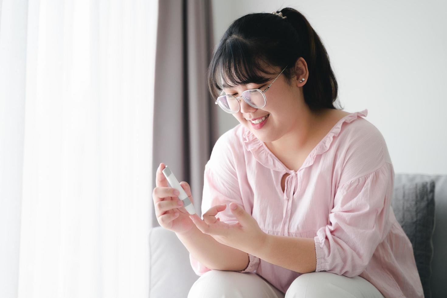 Aziatische vrouw die lancet op vinger gebruikt voor het controleren van de bloedsuikerspiegel door glucosemeter, gezondheidszorg en medisch, diabetes, glycemieconcept foto